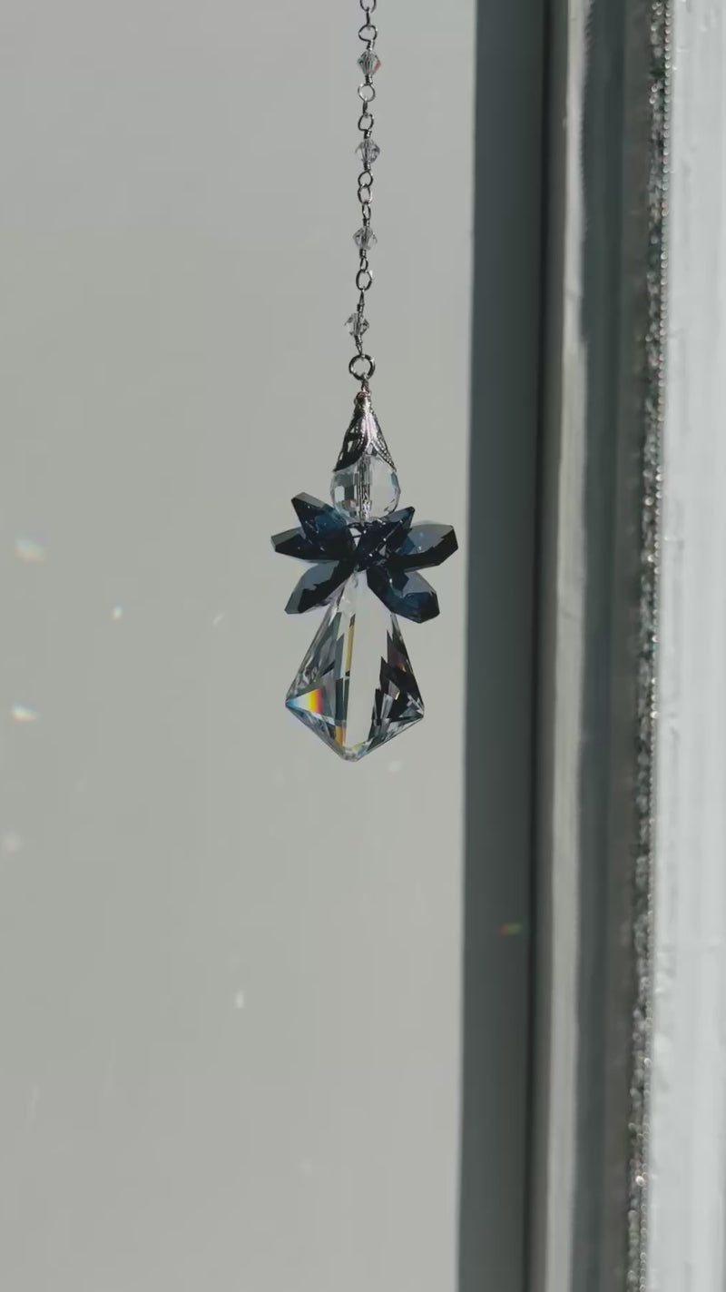 Handcrafted Saphoreus wizard angel crystal suncatcher twisting gently indoors, highlighting the deep sapphire blue glass wings and faceted clear glass body.