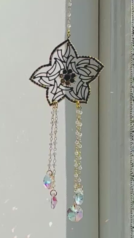Handcrafted Winter's Gold crystal suncatcher spinning gently indoors next to a window, casting vibrant iridescent rainbow prisms across the wall.
