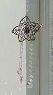 Handcrafted Winter's Gold crystal suncatcher spinning gently indoors next to a window, casting vibrant iridescent rainbow prisms across the wall.