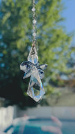 Handcrafted Saphoreus wizard angel crystal suncatcher spinning gently, showing a side view of its sapphire blue wings and faceted clear crystal body.