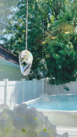A large suncatcher with a colorful Swarovski crystal sparkling as it is spinning in a bright window casting its own reflection.